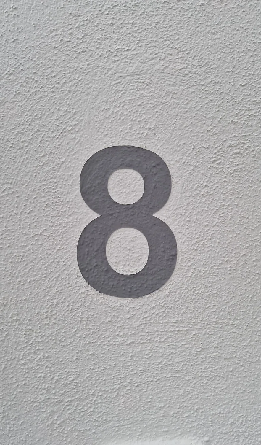 Karl Hansel Inh – Baudekoration – Eine auffällige graue „8“, aufgemalt auf einer strukturierten weißen Wand.