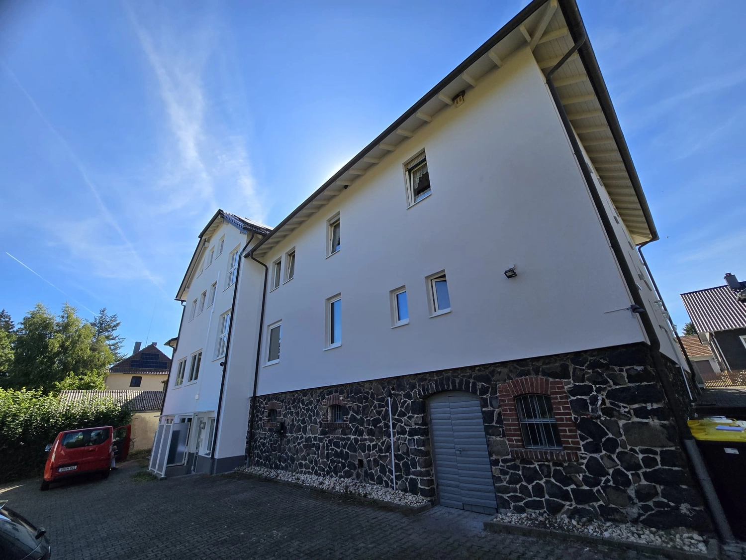 Karl Hansel Inh – Baudekoration – Ein weißes, dreistöckiges Gebäude mit einem Sockel aus Stein, großen Fenstern und einem strahlend blauen Himmel darüber.