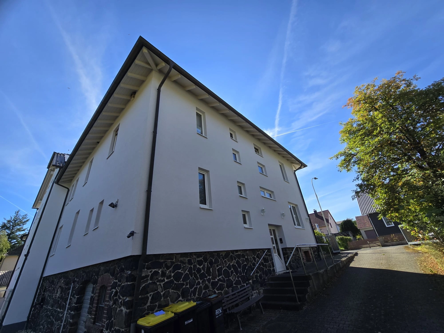 Karl Hansel Inh – Baudekoration – Ein weißes, mehrstöckiges Gebäude mit einem Sockel aus Stein, aus einem niedrigen Blickwinkel unter strahlend blauem Himmel aufgenommen.