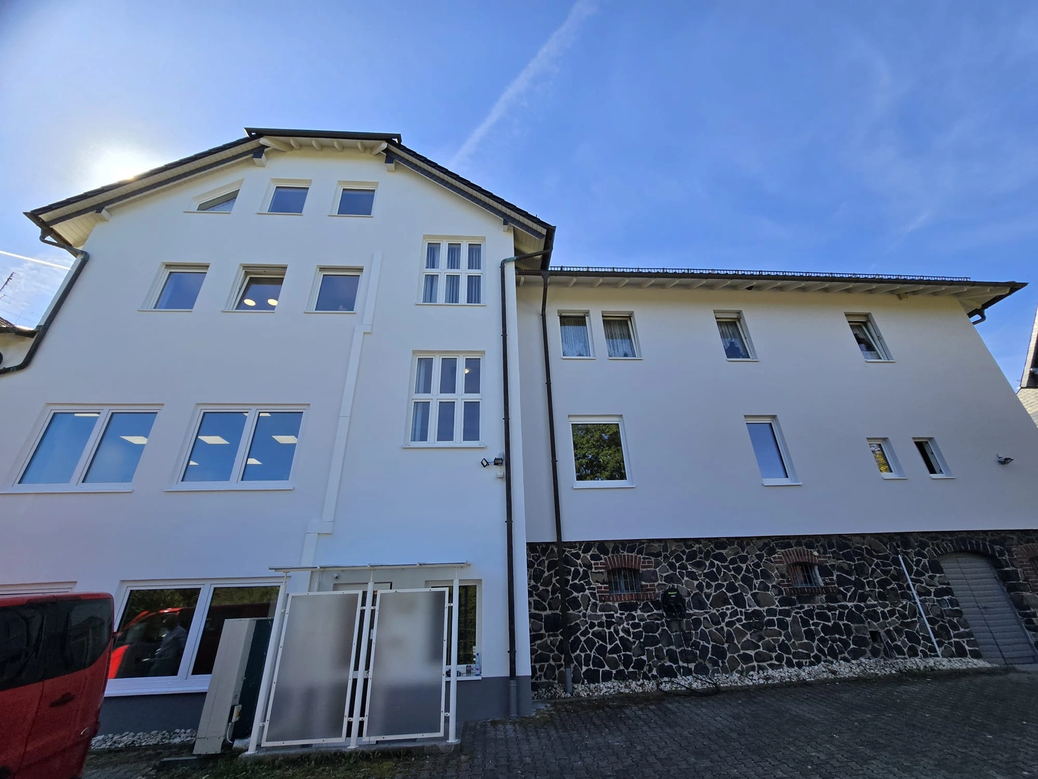 Karl Hansel Inh – Baudekoration – Ein weißes, dreistöckiges Gebäude mit einem Sockel aus Stein, großen Fenstern und einem strahlend blauen Himmel darüber.